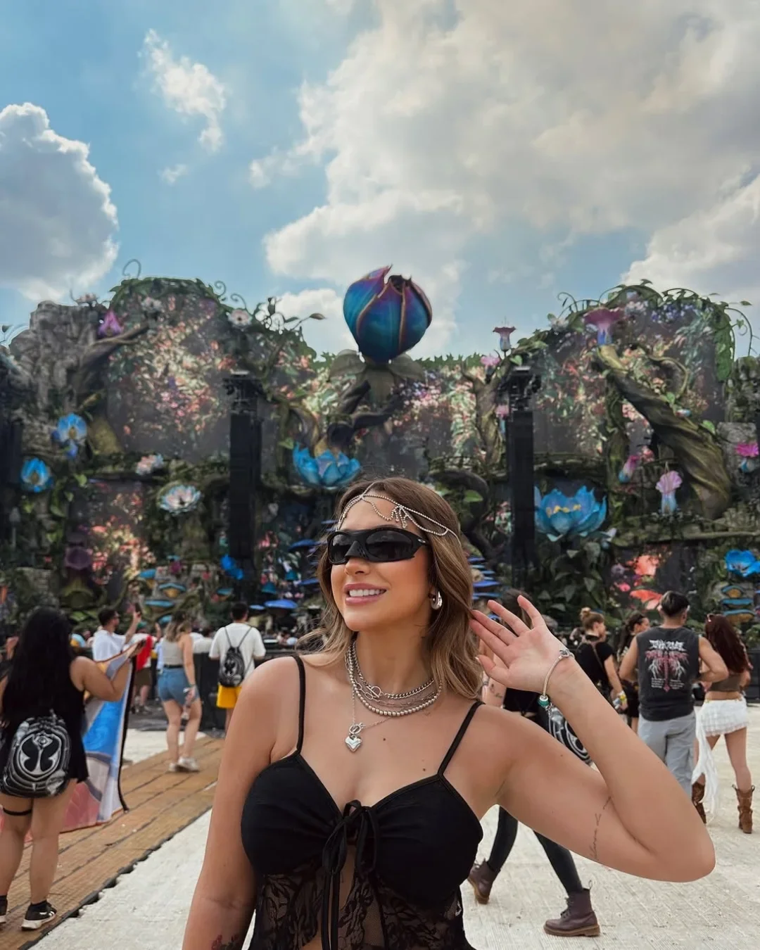 Moça de óculos escuro num festival, com o palco atrás